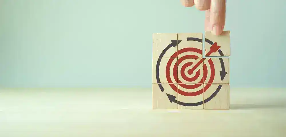 Hand placing wooden blocks with target and arrow symbols, illustrating retargeting strategies.